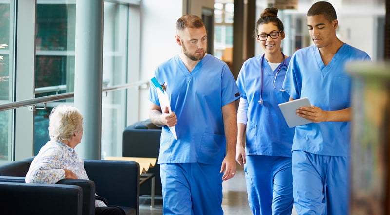 Three junior doctors walking along a hospital corridor, discussing case and wearing scrubs.
