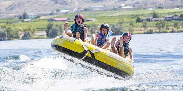 Kids ride in tube, crossing lake behind boat