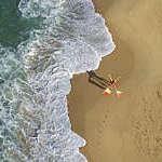 Areal view from a beach where you can see a lifeguard walking with one red and yellow safety flag on each shoulder crossing behind his neck. 