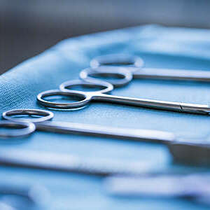 Close-up of three pairs of surgical scissors laid out on a blue sterilization wrap.